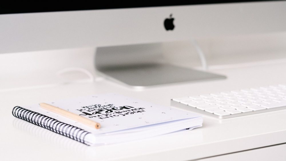mac computer with journal and pen